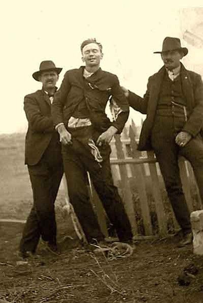 The outlaw John Shaw removed from his coffin and propped up against a picket fence for one last drink of whiskey with his buddies. 